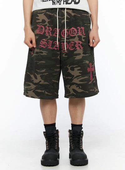 LEWKIN Men's Camo Graphic Sweat Shorts (Dark Green) IL514 Dark green front view on model wearing black boots with pink Dragon Slayer old-english print