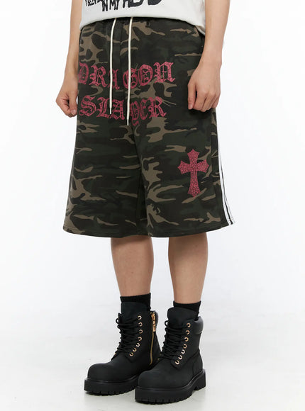 Men's Camo Graphic Sweat Shorts (Dark Green) IL514 Dark green close-up front view on model showing Dragon Slayer pink old-english print cross graphic and drawstring waist