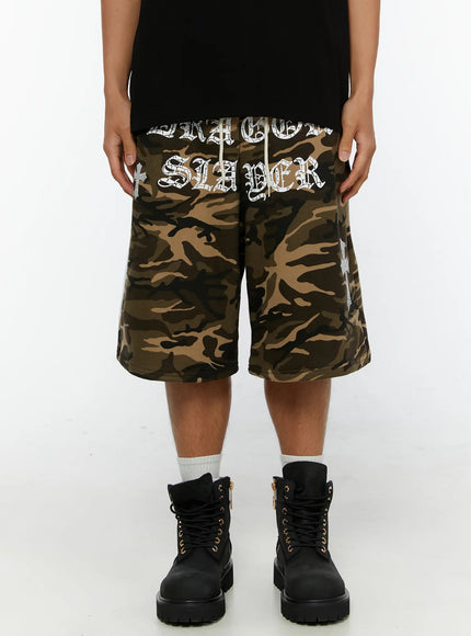 LEWKIN Men's Camo Graphic Sweat Shorts IL515 Beige M/L front view on model wearing black tee and boots, old English DRAGON SLAYER graphic print