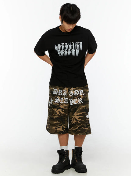 Men's Camo Graphic Sweat Shorts IL515 Beige full-body front view on model looking down, styled with black graphic tee and chunky boots