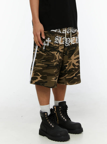 Men's Camo Graphic Sweat Shorts IL515 Beige opposite side view on model showing cross graphic and white double side stripes with black boots