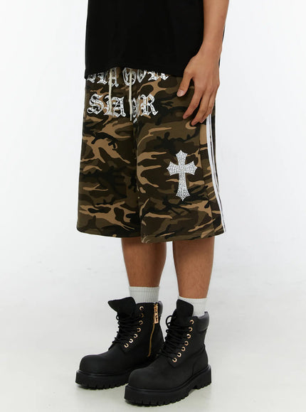 Men's Camo Graphic Sweat Shorts IL515 Beige angled side-front view on model showing crackle cross graphic and white side stripe detail