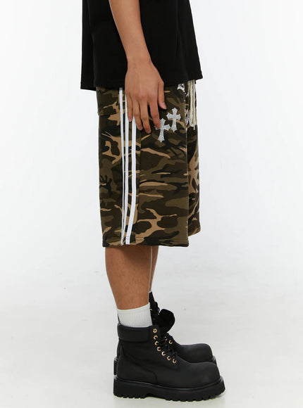 Men's Camo Graphic Sweat Shorts IL515 Beige side view on model highlighting white double stripe tape along leg seam and rhinestone cross graphic