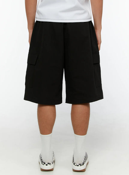 Men's Cargo Bermuda Shorts IL513 Black back view on male model showing clean rear panel, side cargo pockets visible, elastic waistband, and checkered sneakers