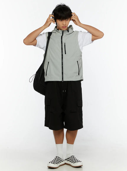 Men's Cargo Bermuda Shorts IL513 Black full-body front styling shot on male model with gray hooded vest, black backpack, and headphones, streetwear outfit