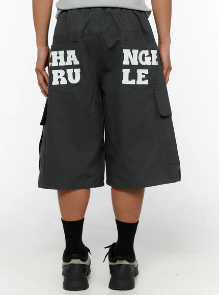 Men's Cargo Jorts IL510 Dark gray three-quarter back view on male model hand in pocket showing CHANGE RULE graphic print and cargo pocket detail