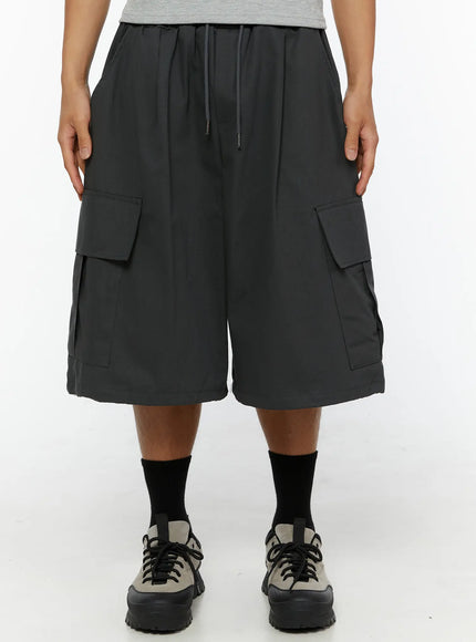 Men's Cargo Jorts IL510 Dark gray front close-up on male model showing drawstring elastic waistband dual cargo flap pockets wide-leg silhouette