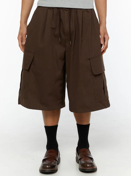 Men's Cargo Pocket Jorts IL510 Dark brown front close-up on model showing drawstring elastic waistband and large flap cargo pockets on wide-leg silhouette