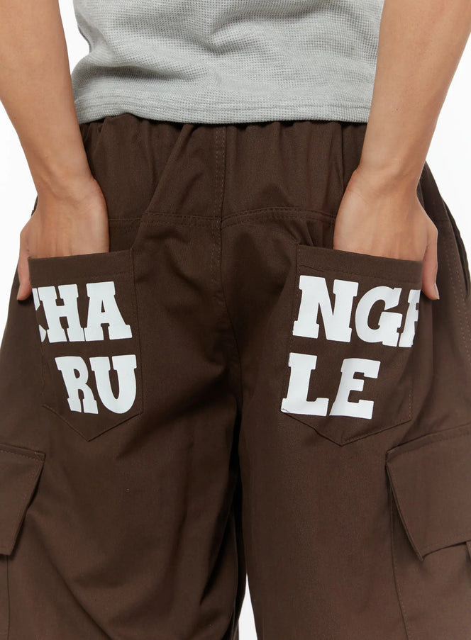 LEWKIN Men's Cargo Pocket Jorts IL510 Dark brown close-up back detail showing white CHANGE RULE graphic print on rear pockets with elastic waistband and cargo pockets visible