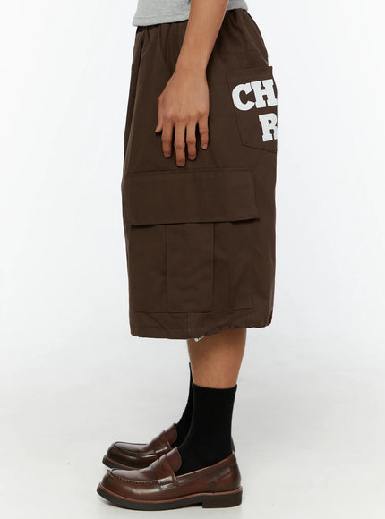 Men's Cargo Pocket Jorts IL510 Dark brown side view on model showing white CHANGE RULE graphic print on back pocket and large flap cargo pocket on oversized hem