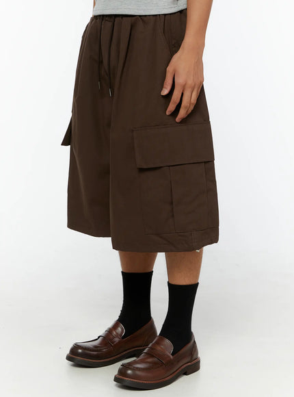 Men's Cargo Pocket Jorts IL510 Dark brown side view on model highlighting right cargo pocket and partial white graphic print with drawstring waist and loafers