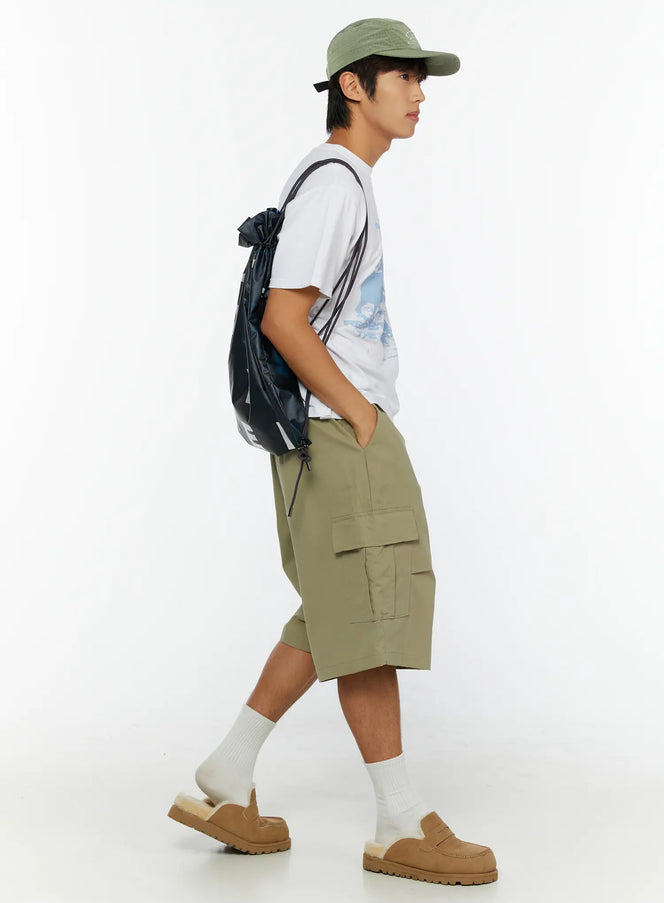 Men's Cargo Shorts IL513 Dark green side full-body view on male model walking, green cap and black drawstring backpack, cargo pocket detail visible