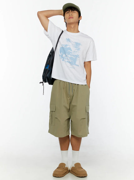 Men's Cargo Shorts IL513 Dark green full-body front view on male model hand behind head, green cap, black shoulder bag, relaxed cargo shorts styling