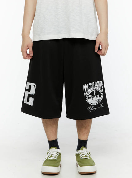 LEWKIN Men's Casual Number Print Shorts (Black) IL509 Black M/L front view on model wearing white tee and green sneakers, wide-leg silhouette with collegiate graphic print