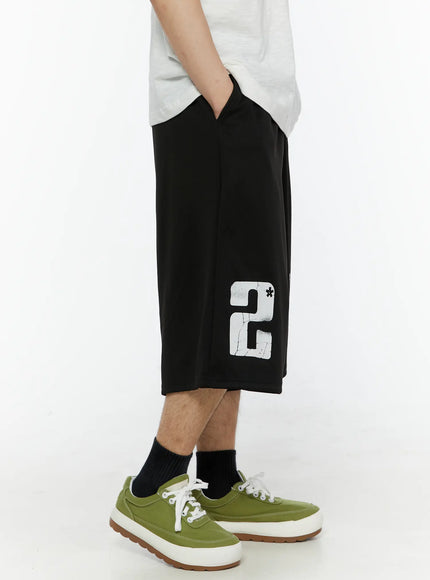 Men's Casual Number Print Shorts (Black) IL509 Black opposite side view on model showing large distressed number 2 graphic print on left leg, wide-leg cut with green sneakers