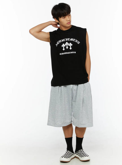 Men's Casual Sweat Shorts IL510 gray full-body shot on male model with hand raised to neck in relaxed pose, showing pleated front and wide-leg length with checkered sneakers