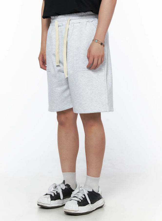 Men's Casual Sweat Shorts (Light Gray) IL502 Light Gray side view on model showing patch pocket detail, cream drawstring, elastic waist, heathered fleece texture, styled with black tee