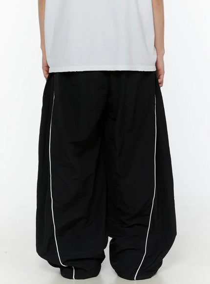 Men's Contrast Piping Nylon Track Pants (Black) IL507 Black back view on model showing elastic waistband, dual white piping on both legs, and gathered hem