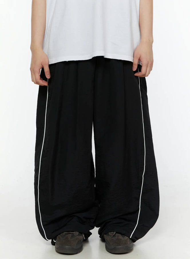 LEWKIN Men's Contrast Piping Nylon Track Pants (Black) IL507 Black S(F1) front close-up on model pulling waistband, wide-leg silhouette with white side piping
