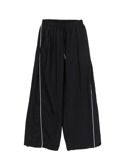 Men's Contrast Piping Nylon Track Pants (Black) IL507 Black flat-lay front view showing elastic drawstring waist, white side piping, wide-leg cut, and hem drawcord