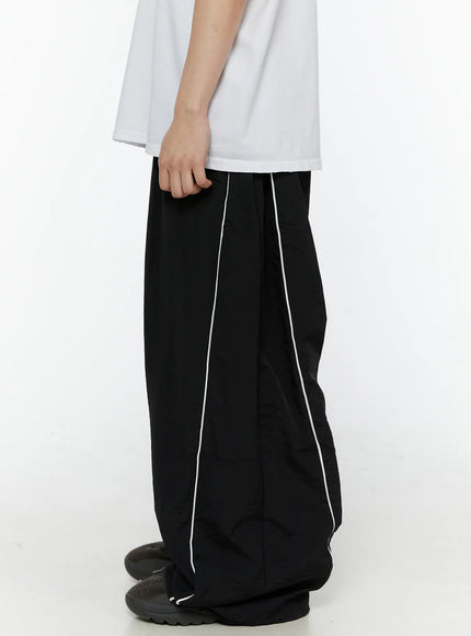 Men's Contrast Piping Nylon Track Pants (Black) IL507 Black side close-up on model showing double white piping lines along outer leg and gathered ankle hem