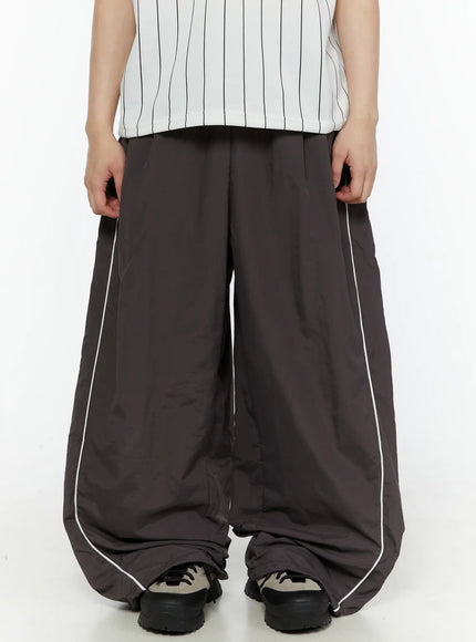 LEWKIN Men's Contrast Piping Nylon Track Pants (Dark Gray) IL507 Dark gray front close-up on model showing wide-leg silhouette and white piping detail paired with striped top and chunky sneakers