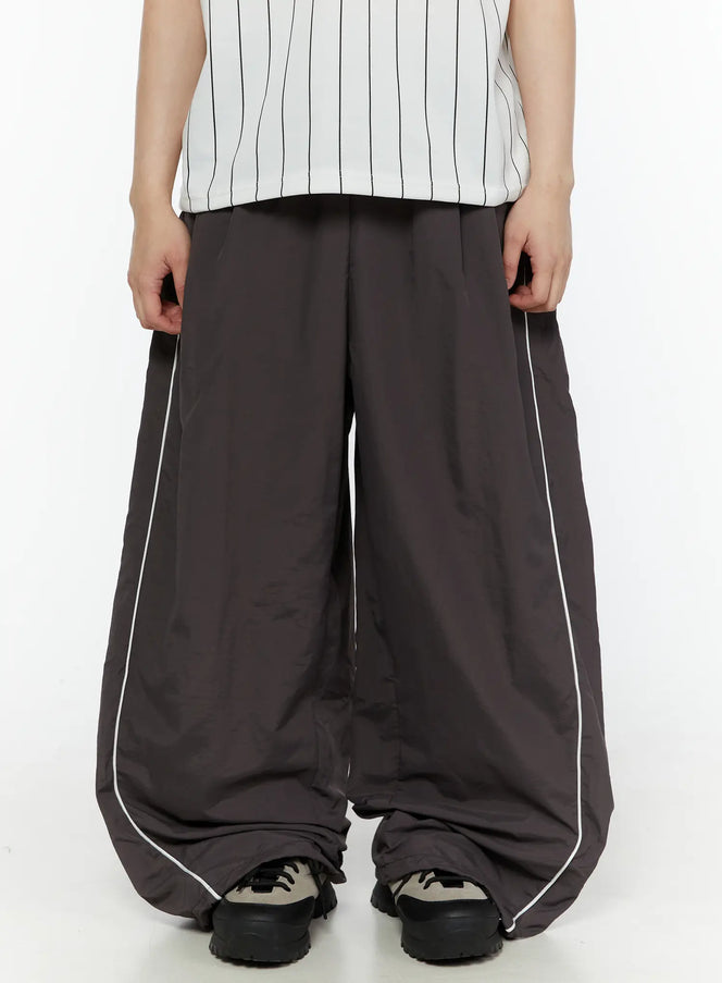 LEWKIN Men's Contrast Piping Nylon Track Pants (Dark Gray) IL507 Dark gray front close-up on model showing wide-leg silhouette and white piping detail paired with striped top and chunky sneakers