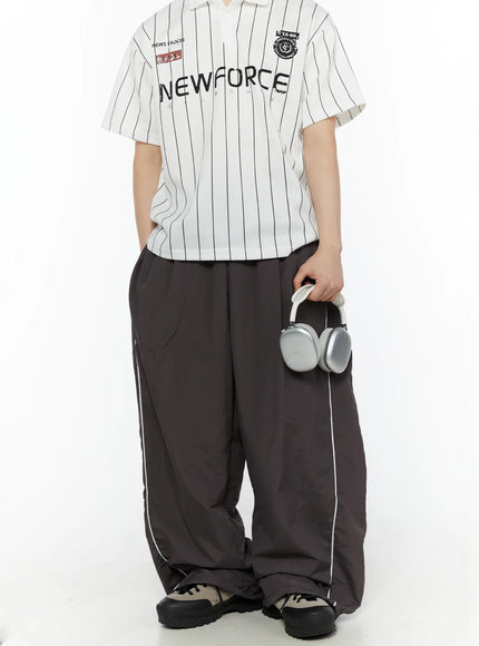 Men's Contrast Piping Nylon Track Pants (Dark Gray) IL507 Dark gray full-body front shot on model styled with striped polo and chunky sneakers holding silver headphones