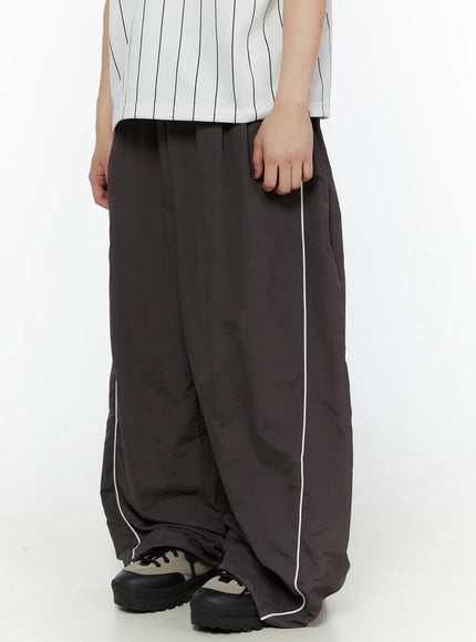 Men's Contrast Piping Nylon Track Pants (Dark Gray) IL507 Dark gray side close-up on model showing white contrast piping along leg seam and voluminous wide-leg nylon fabric