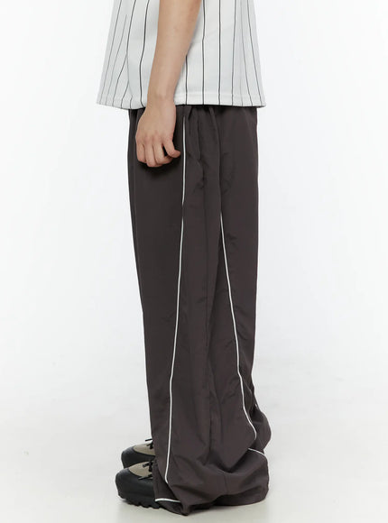 Men's Contrast Piping Nylon Track Pants (Dark Gray) IL507 Dark gray side shot on model showing drawstring waist elastic waistband and white piping running down wide-leg nylon panels