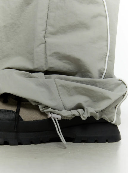 Men's Contrast Piping Nylon Track Pants (Gray) IL507 Gray close-up detail of adjustable drawstring hem with toggle cinch and crinkled nylon texture at ankle