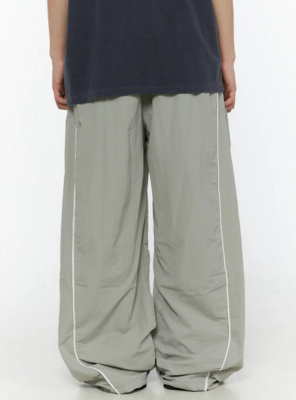 Men's Contrast Piping Nylon Track Pants (Gray) IL507 Gray back shot on model showing rear panel white contrast piping seams and gathered nylon hem pooling at floor