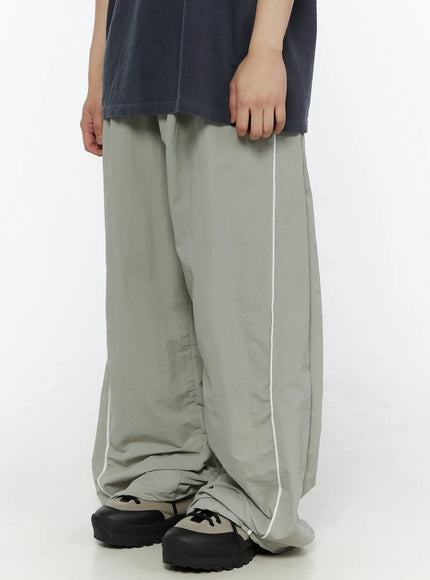 Men's Contrast Piping Nylon Track Pants (Gray) IL507 Gray front side shot on model highlighting wide-leg volume and white piping along outer seam above sneakers