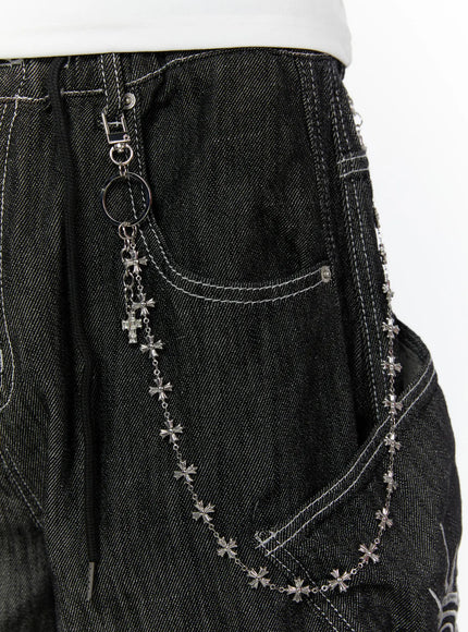LEWKIN Men's Cross-Link Chain IL509 Silver close-up detail shot clipped to dark denim waistband showing cross charm pendant and draped chain across front pocket