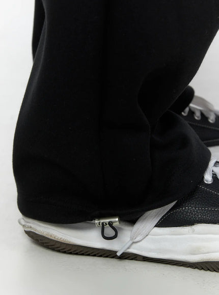 Men's Curved Fit Sweatpants (Black) IL502 black close-up detail of hem zipper puller on wide-leg trouser leg showing soft fleece texture
