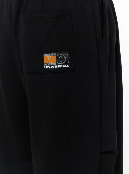 Men's Curved Fit Sweatpants (Black) IL502 black close-up detail of GT 91 UNIVERSAL woven badge patch on side cargo pocket