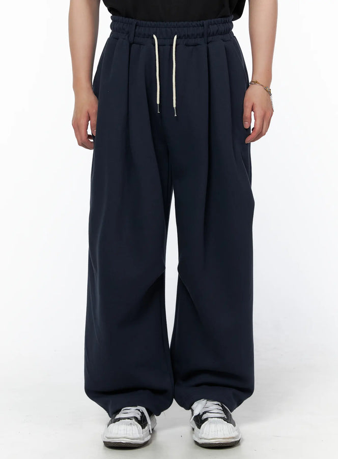 Men's Curved Fit Sweatpants (Dark Blue) IL502 Dark blue front close-up on model showing cream drawstring elastic waistband and pleated wide-leg cut