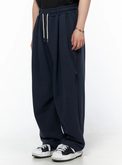 Men's Curved Fit Sweatpants (Dark Blue) IL502 Dark blue side close-up on model highlighting pleated waistband cream drawstring and relaxed wide-leg drape