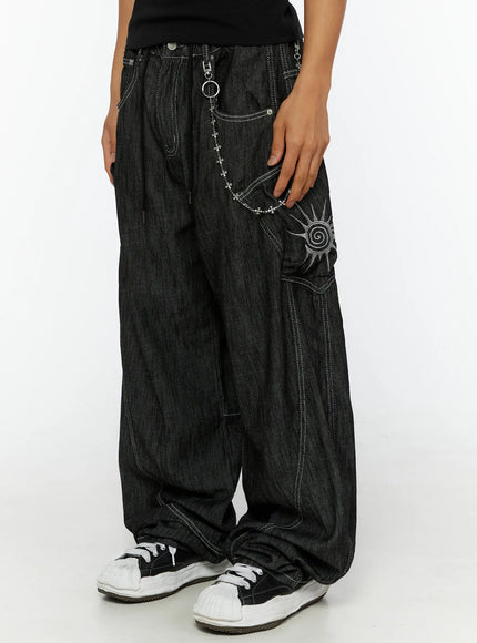 LEWKIN Men's Dale Embroidered Baggy Jeans IL509 black close-up side view on female model hand in pocket showing sun embroidery and silver chain detail