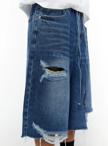 Men's Distressed Jorts IL509 Blue close-up detail shot on model showing large ripped thigh hole with frayed drawstring and raw cut hem