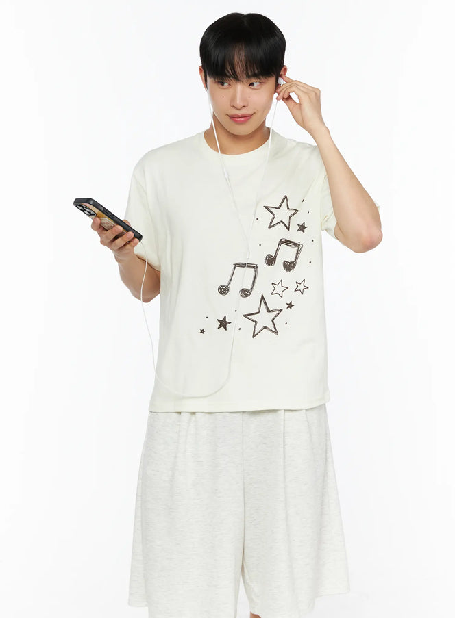 LEWKIN Men's Drawing Graphic Tee IL514 Light yellow front shot on male model holding phone with earphones, star and music note print, size S/M