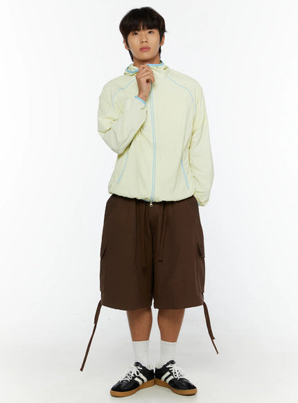 Men's Drawstring Cargo Shorts IL515 Brown full-body front shot on male model holding zipper of yellow windbreaker with loose drawstrings hanging