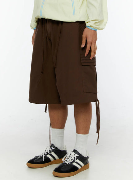 Men's Drawstring Cargo Shorts IL515 Brown three-quarter front shot on model showing right-side cargo pocket with ribbed strap detail and side drawstring