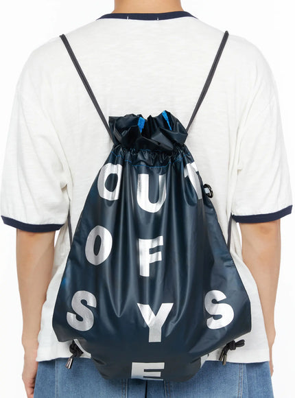 Men's Drawstring String Bag IL510 Navy back view worn on male model in white tee and jeans showing silver letter graphic and blue accent stitching