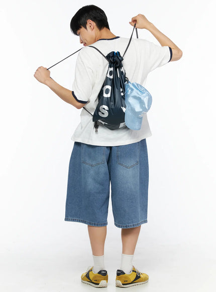 Men's Drawstring String Bag IL510 Navy back view on male model pulling drawstrings open wearing white tee and denim shorts with light blue cap attached
