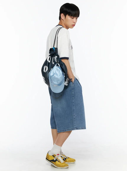 Men's Drawstring String Bag IL510 Navy side view on male model carrying bag on one side in white tee and wide denim shorts looking downward