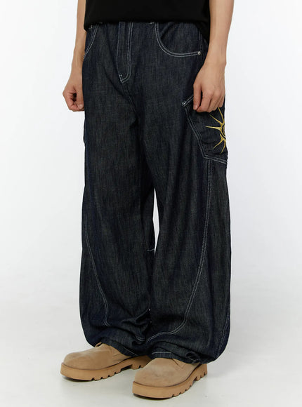 Men's Embroidered Wide Leg Jeans IU529 Dark blue front cropped waist-down on model, showing cargo pocket with partial gold sun embroidery and curved contrast stitching