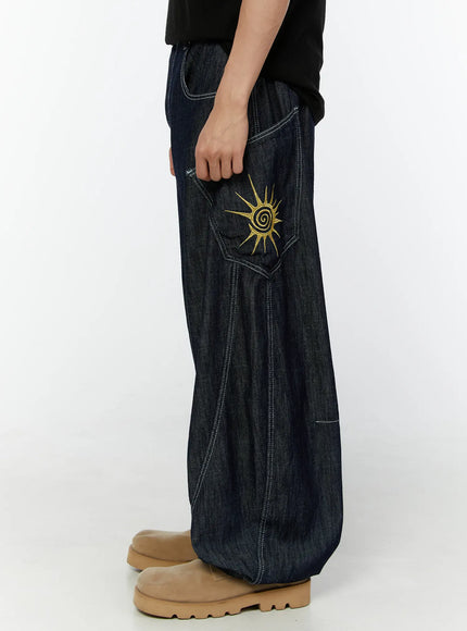 Men's Embroidered Wide Leg Jeans IU529 Dark blue side profile full-length on model, hand in pocket, gold sun embroidery visible on side cargo pocket, beige boots