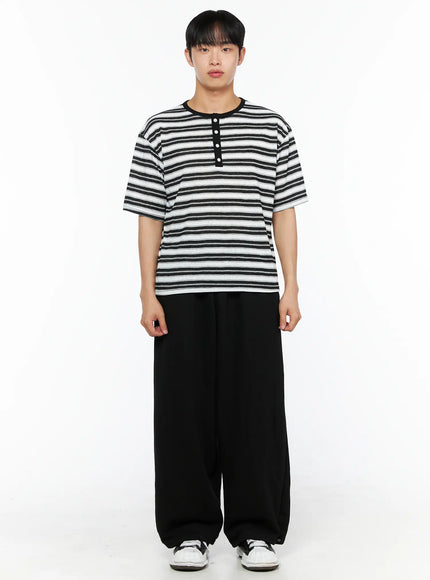 Men's Flame Wide Sweatpants (Black) IL514 front view full body on male model standing straight, paired with black and white stripe henley tee and white sneakers