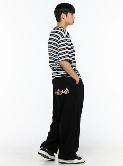 Men's Flame Wide Sweatpants (Black) IL514 side view on male model standing with hands in pockets, styled with black and white striped henley tee and sneakers